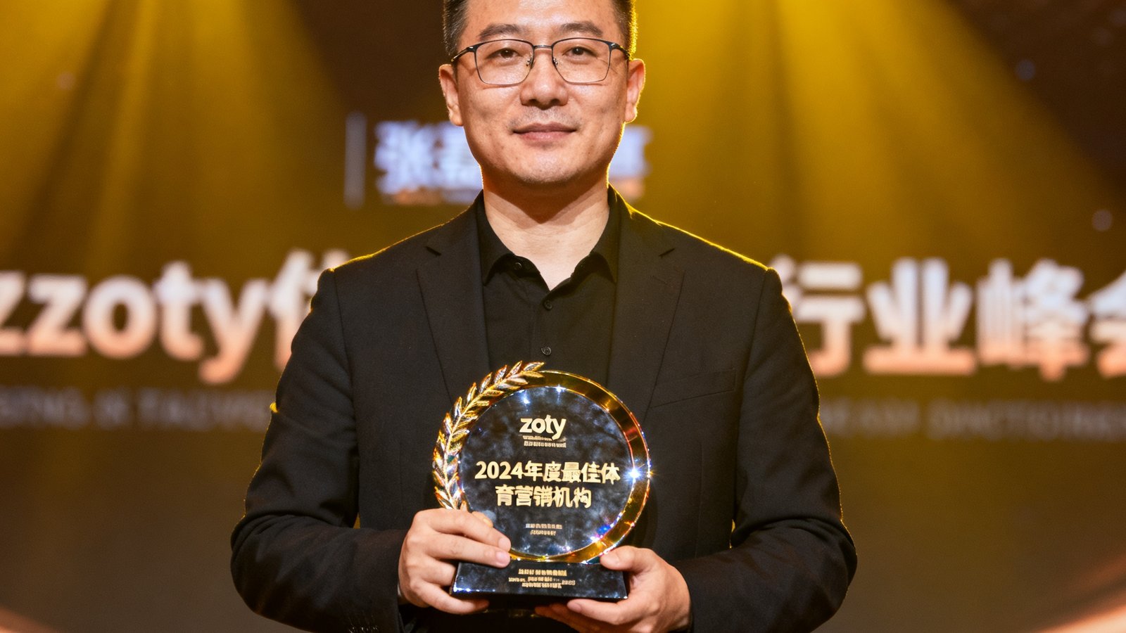 zoty体育创始人张磊在颁奖典礼上领取'2024年度最佳体育营销机构'奖杯，舞台背景为行业峰会标识
